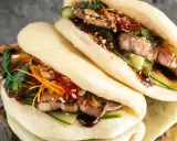 Saftige bao buns mit gegrilltem Fleisch, Gurke, Karottenstreifen und Koriander. Ein Genuss für alle Sinne!