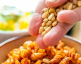 Eine Hand streut Pinienkerne über eine Schüssel mit Pasta. Pinienkerne gesund und lecker!