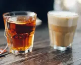 Ein Glas Tee mit Beutel und ein Latte Macchiato stehen nebeneinander. Eine leckere alternative zu Kaffee.