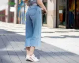 Styling culotte jeans: Ein lässiger Look mit hellblauen Jeans, weißem Shirt und Sneakern auf gepflastertem Weg.