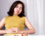 Frau mit schmerzverzerrtem Gesicht hält sich den Bauch. Sie leidet unter Bittertropfen vor oder nach dem Essen.