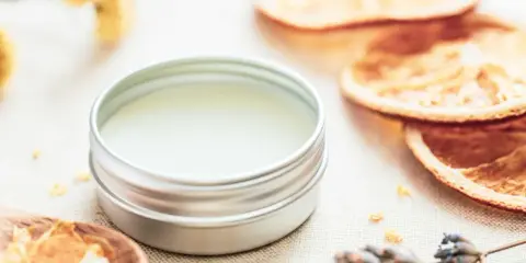 Ein Döschen mit selbstgemachtem Lippenbalsam, umgeben von getrockneten Orangen, Lavendel und Kräutern.