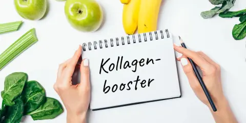Hände halten Notizbuch mit "Kollagen-Booster". Frisches Obst und Gemüse wie Äpfel, Bananen, Sellerie, Spinat und Brokkoli liegen daneben. Eine Kollagen Lebensmittel Tabelle könnte hier inspirieren.