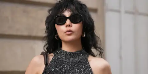 Frau mit schwarzem Wolf Cut Locken, Sonnenbrille und glitzerndem Top.