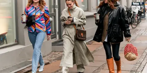 Drei Frauen spazieren mit Kaffee. Die mittlere trägt weite Hosen zu Pumps. Die rechte zeigt, welche Hose zu Boots Damen passt: Leggings und hohe Stiefel.