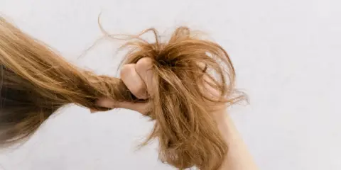 Eine Hand greift nach strohigen Haaren, die trocken und ungepflegt aussehen.