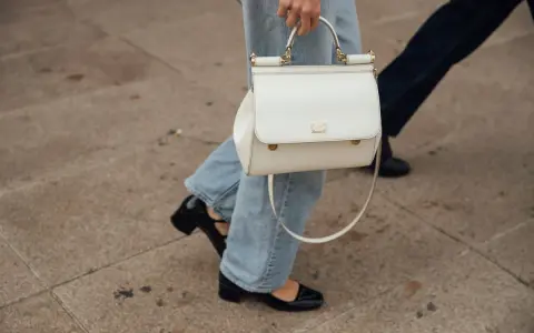 Eine Frau kombiniert lässig wide leg jeans mit schwarzen Lackschuhen und einer weißen Handtasche.