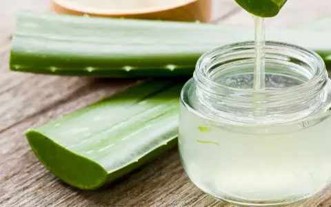 Frische Aloe Vera Blätter und ein Glas mit klarem Saft, der gerade aus einem Blatt getropft wird. Perfekt, um aloe vera saft selber machen.