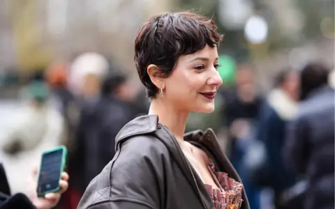 Frau mit einem langen Pixie-Haarschnitt, dunklem Lederjacke und auffälligem Kleid.