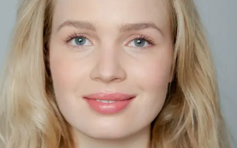 Blonde Frau mit blauen Augen und rosafarbenen Lippen, die frisch aussieht.