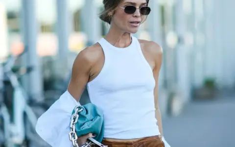 Frau im weißen Tanktop, brauner Lederhose und blauer Tasche. Der "no bra trend" ist hier subtil umgesetzt.