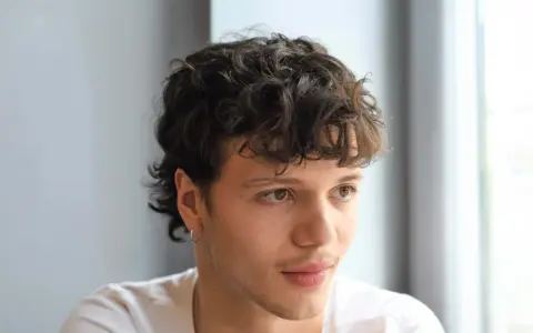 Junger Mann mit lockigem, kurzem Mullet-Haarschnitt und einem dezenten Ringohrring.