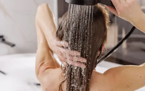 Frau wäscht sich die Haare unter der Dusche, Wasser rinnt über ihre Schultern. Eine sanfte Methode, um die Haare zu reinigen, fast wie haare waschen ohne shampoo.