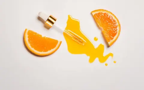 Ein Pipettenfläschchen mit leuchtend gelbem Vitamin C Serum, umgeben von saftigen Orangenscheiben. Morgens oder abends für strahlende Haut.