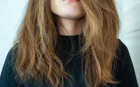 Frau mit zerzaustem, trockenem Haar, das ihr ins Gesicht fällt. Ihre Lippen sind leicht geöffnet und mit rosafarbenem Lippenstift bemalt.