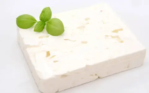 Ein Block Feta-Käse mit Basilikumblättern. Ist Feta gesund? Ja, er liefert Kalzium und Proteine.