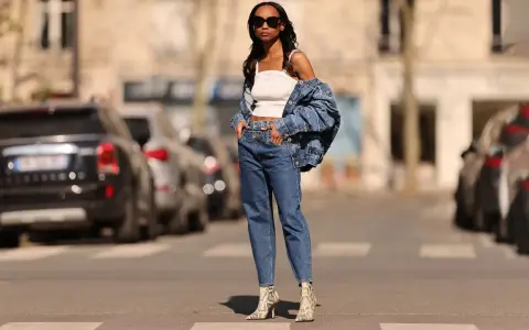 Stylisches Outfit: Eine Frau kombiniert barrel jeans mit einem weißen Top und Jeansjacke. Schlangenleder-Stiefel runden den Look ab.