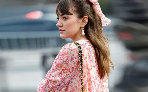 Eine Frau mit einem Blumenkleid und einer einfachen Frisur, perfekt für eine Hochzeitsgast. Ein Scrunchie mit Blumenmuster ziert ihren Pferdeschwanz.