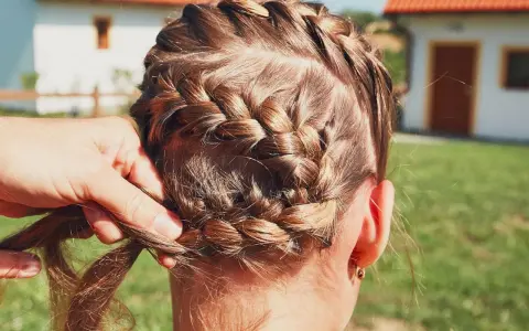 Zopf flechten für Oktoberfest Frisuren einfach. Eine Hand flechtet das braune Haar zu einem kunstvollen Zopf.