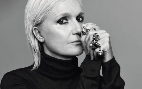 Maria Grazia Chiuri, mit markantem Make-up und vielen Ringen, blickt nachdenklich in die Kamera.