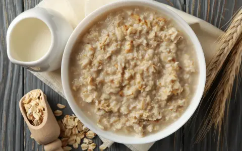 Schüssel mit Haferflocken, daneben ein Milchkännchen, Holzschaufel mit Haferflocken und Ähren. Die Haferflocken Inhaltsstoffe sind hier gut sichtbar.