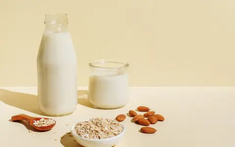 Flasche und Glas mit milchigem Getränk, daneben Mandeln und Haferflocken. Ob Mandelmilch oder Hafermilch, die Wahl ist leicht.