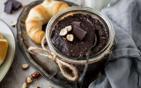 Selbstgemachte Haselnusscreme im Glas, garniert mit Schokostückchen und Nüssen, neben einem Croissant. Perfekt zum Haselnusscreme selber machen!