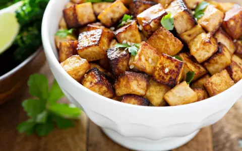 Knusprig gebratene Tofuwürfel in einer weißen Schüssel. Sie sehen lecker aus und man fragt sich, wie schmeckt tofu, wenn er so zubereitet wird.
