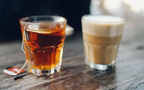 Ein Glas Tee mit Beutel und ein Latte Macchiato stehen nebeneinander. Eine leckere alternative zu Kaffee.