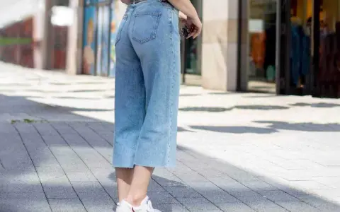Styling culotte jeans: Ein lässiger Look mit hellblauen Jeans, weißem Shirt und Sneakern auf gepflastertem Weg.