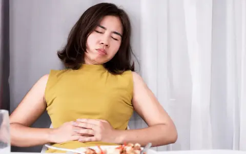 Frau mit schmerzverzerrtem Gesicht hält sich den Bauch. Sie leidet unter Bittertropfen vor oder nach dem Essen.