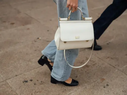Eine Frau kombiniert lässig wide leg jeans mit schwarzen Lackschuhen und einer weißen Handtasche.