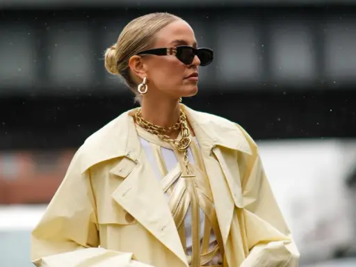 Stylische Frau mit Dutt, Sonnenbrille und auffälligem Schmuck. Eine perfekte Frisur, die auch bei fettigen Haaren gut aussieht.