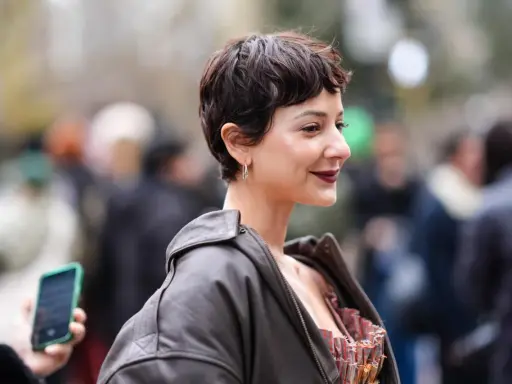 Frau mit einem langen Pixie-Haarschnitt, dunklem Lederjacke und auffälligem Kleid.