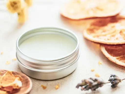 Ein Döschen mit selbstgemachtem Lippenbalsam, umgeben von getrockneten Orangen, Lavendel und Kräutern.