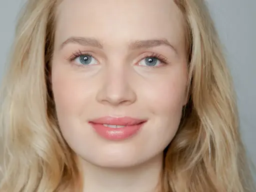 Blonde Frau mit blauen Augen und rosafarbenen Lippen, die frisch aussieht.