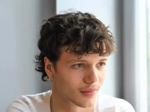 Junger Mann mit lockigem, kurzem Mullet-Haarschnitt und einem dezenten Ringohrring.