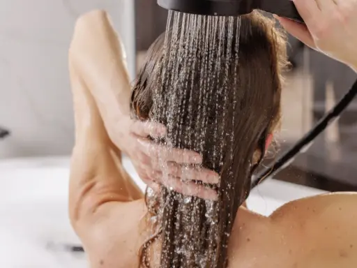 Frau wäscht sich die Haare unter der Dusche, Wasser rinnt über ihre Schultern. Eine sanfte Methode, um die Haare zu reinigen, fast wie haare waschen ohne shampoo.