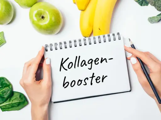 Hände halten Notizbuch mit "Kollagen-Booster". Frisches Obst und Gemüse wie Äpfel, Bananen, Sellerie, Spinat und Brokkoli liegen daneben. Eine Kollagen Lebensmittel Tabelle könnte hier inspirieren.
