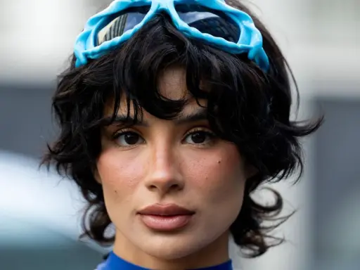 Ein Model mit einer shixie Frisur und blauen Skibrillen auf dem Kopf.