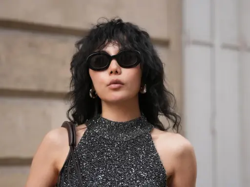 Frau mit schwarzem Wolf Cut Locken, Sonnenbrille und glitzerndem Top.