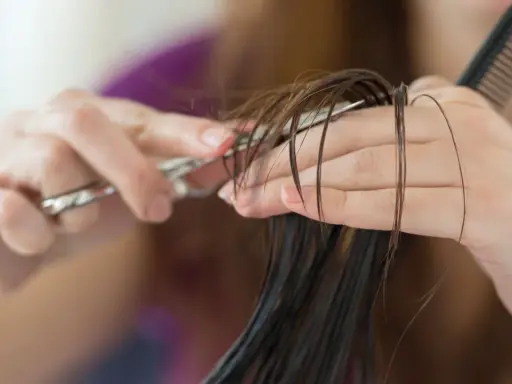 Hände schneiden feuchtes Haar mit einer Schere. Ein Kamm liegt bereit für den nächsten Schritt des jellyfish cut.