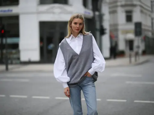 Stylische Frau in grauem Pullunder, weißer Bluse und Jeans. So lässt sich ein Pullunder kombinieren für einen lässigen Look.