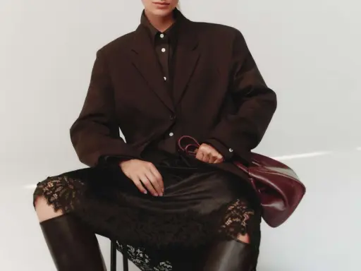 Elegant outfit: braun und schwarz kombinieren mit einem braunen Blazer, schwarzer Spitzenrock und Lederstiefel. Eine Hand hält eine weinrote Tasche.