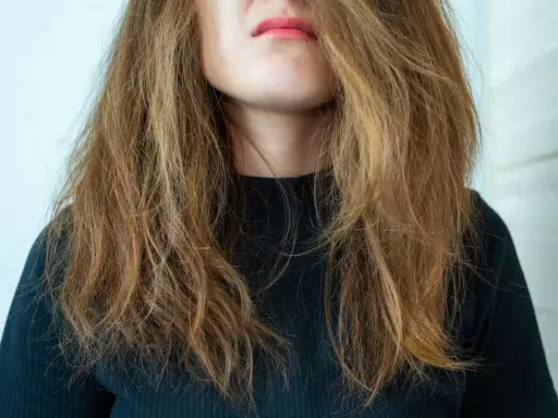 Frau mit zerzaustem, trockenem Haar, das ihr ins Gesicht fällt. Ihre Lippen sind leicht geöffnet und mit rosafarbenem Lippenstift bemalt.