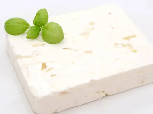 Ein Block Feta-Käse mit Basilikumblättern. Ist Feta gesund? Ja, er liefert Kalzium und Proteine.