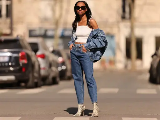 Stylisches Outfit: Eine Frau kombiniert barrel jeans mit einem weißen Top und Jeansjacke. Schlangenleder-Stiefel runden den Look ab.