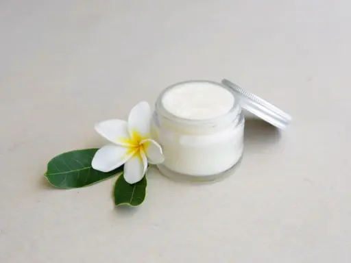 Creme in einem Glas mit einer Blüte und Blättern. Perfekt, um Deo selber machen mit Sheabutter.