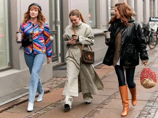 Drei Frauen spazieren mit Kaffee. Die mittlere trägt weite Hosen zu Pumps. Die rechte zeigt, welche Hose zu Boots Damen passt: Leggings und hohe Stiefel.