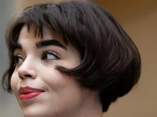 Eine Frau mit einem eleganten, dunklen short bob und rotem Lippenstift blickt nach links.